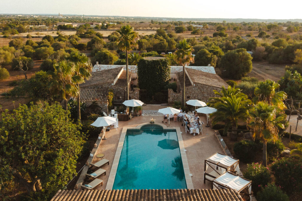 Drohnenaufnahme von einer Hochzeitslocation auf Mallorca. Es zeigt den Dinnertisch am Pool mit Gästen.